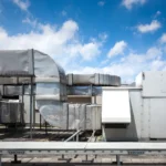 square-airconditioning-unit-roof-with-round-fan-background-gradually-receding-other-units-that-are-out-focus-right-side-light-blue-sky-commercial-space